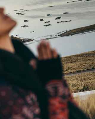 Tilted view of Lake Titicaca's floating islands and grass plains, obscured by a woman with hands together in soft-focus.