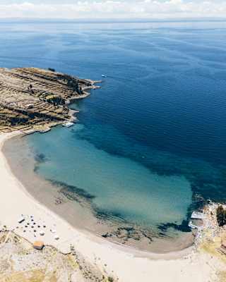 Breathtaking aerial view of the white-sand sweep and clear blue waters of Collata Beach on Lake Titicaca's Taquile Island.