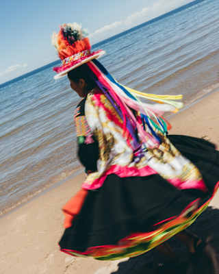 A woman in traditional dress dances on Collata Beach, her black skirt twirling and her hat streaming with bright ribbons.