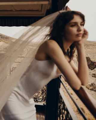 In soft-focus, a bride leans forward on the observation deck rail, propping her chin in a hand as she gazes at the landscape.