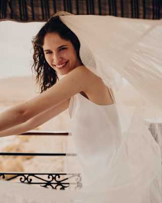 A dark-haired bride smiles to camera as she stands in a white dress on the Observation Car deck, veil billowing behind her.