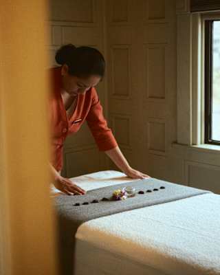 A spa therapist in a deep-orange uniform smooths out the cloth on a table topped with a line of stones set on a grey throw.