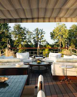 View across Coquelicot's luxurious deck with two white corner sofas and armchairs, a drinks table, lighting and plant pots.