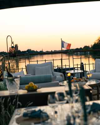 Looking over a dining table in soft-focus to the seating area, where a small French flag flies against the peachy sunset sky.