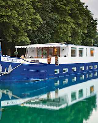 Exterior of a royal-blue bottomed river barge moored alongside a tree-lined canal