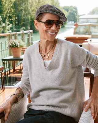 Chef Dominique Crenn, in dark glasses, cap and grey jumper, smiles as she sits on the deck of a bateau on a sunny waterway.