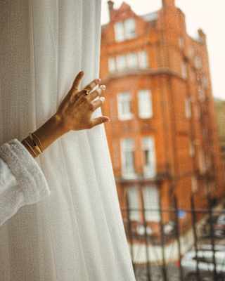 The hand of a female guest pulls back a curtain to reveal a view of the grand red-brick Victorian London townhouse opposite.