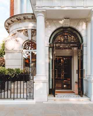 Beneath a white stone portico, The Cadogan Hotel's logoed wood and glass doors open to a glimpse of the gleaming interior.