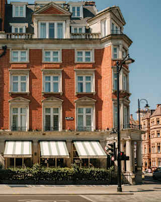 View of The Cadogan with rows of white-framed windows set in a red brick façade above a portico and three restaurant awnings.