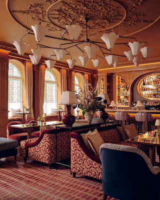 A collection of sofas, chairs and tables promotes relaxation in a lounge with a gleaming bar, chandelier and honey-tone décor.