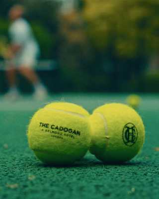 Close-up of two yellow tennis balls on a court, one stencilled with the words The Cadogan and the other with the hotel logo.