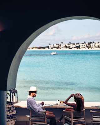 A smiling couple sitting at a restaurant counter table on an open-air terrace overlooking the Caribbean sea