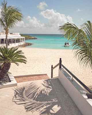 Palms cast feather shadows on steps leading from Cap Juluca to the white-sand beach, with a glimpse of Cip's on the rocks.