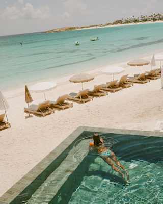 High angle shot in soft hues of a woman floating in the emerald water of Uchu's infinity pool overlooking the beach and sea.