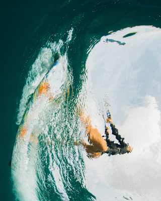 Ninety-degrees rotated shot taken below the water, looking up through the surface at woman kitesurfing, her image distorted.