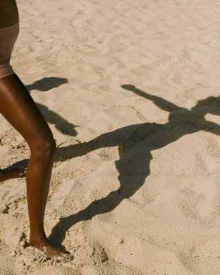 A  woman, off-camera, casts a shadow on the rippled white beach sand as she poses in warrior position during a yoga session.