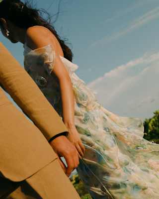 Angled image of a man in a mustard suit, from the waist down, and a woman behind with dark hair and a floaty pastel dress.