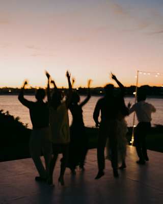 Looking at the silhouettes of dancers with their arms in the air as the sun sets at an evening event overlooking the bay.