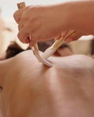 A therapist applies two brushes to a guest's back, stroking them in opposite directions, seen close-up in a spa detail.