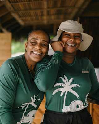Barbie Mora and Karol Piña, The Cap Shack Servers, laugh together facing the camera, wearing Cap Juluca green tops.