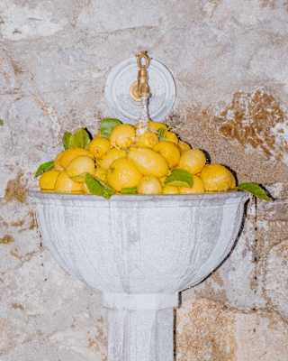 A mountain of lemons fills a marble sink set into a stone exterior wall as a running tap overflows