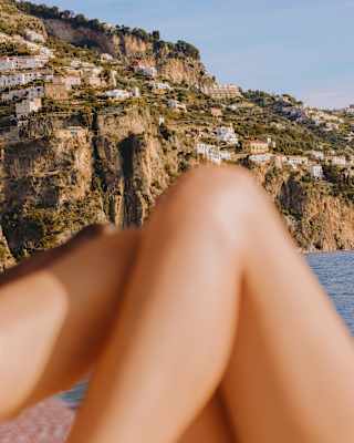 Above sunbathing knees, houses perch on the top of limestone cliffs that plunge dramatically into the Tyrrhenian Sea