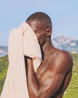A young man dries his face with a peach-coloured towel before the distant jagged limestone peaks of the Lattari Mountains
