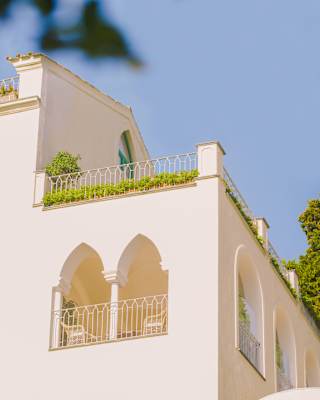 Neatly tended terracotta planters trace the edge of a railing edged balcony, adding fresh green to white walls and blue sky