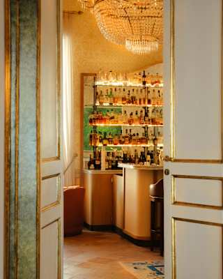 View through partly-open doors into a room with a crystal chandelier and a bar with bottle shelves with LED strip lights.