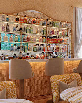 Ochre-veined marble tables with complementary tub chairs fill a bar lounge with a cane-fronted bar, stools and bottle shelves.