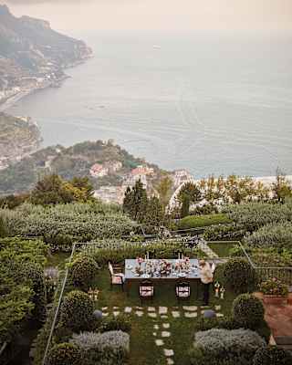 Outdoor table coated in flowers and candles overlooking lush hillside gardens
