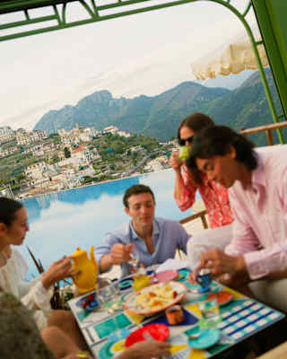Angled shot of a group of guests in soft-focus as they enjoy food at the infinity pool bar with a Lattari mountains backdrop.