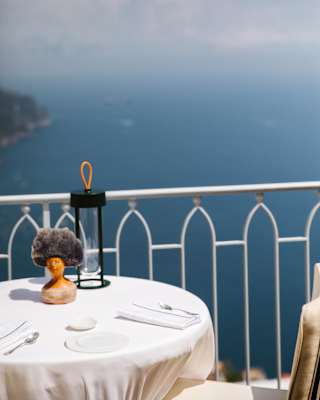 View from Belvedere's terrace, over a white dining table, through elegant railings into the deep blue water of Amalfi's sea.