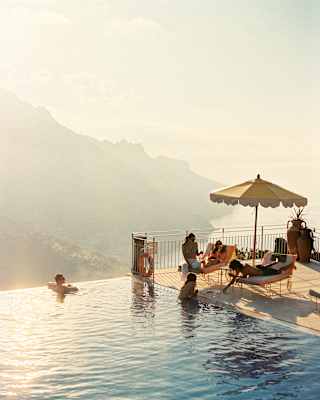 Two guests swim in the gold-tinted waters of the pool as they chat to three more who relax on loungers, seen from above.
