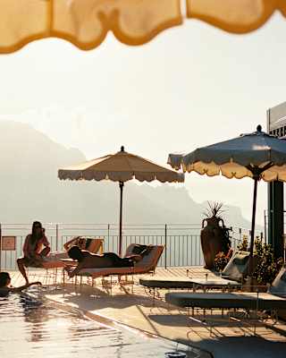 Two friends relax in the pool and chat to three more who sit on loungers enjoying the views and perks of the La Piscina club.