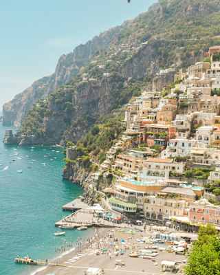 The peach-pastel buildings of Positano climb steep cliffs overlooking a busy beach and azure sea filled with pleasure boats.