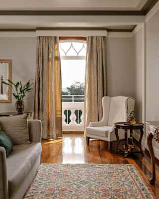 View over an antique rug and glossy, polished floorboards to an open door to a terrace flanked by long wheat-toned drapes.