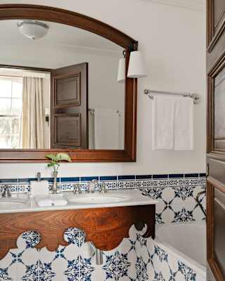 A wood-framed wall mirror reflects a window in a Junior Suite bathroom with a marble basin unit with blue and white tiling.