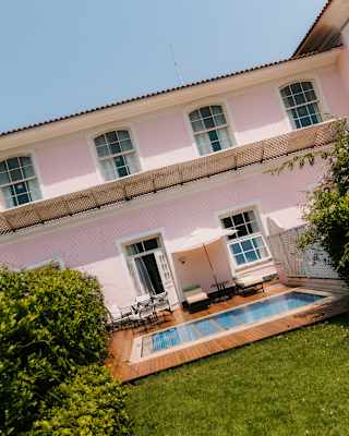 Loungers recline by a blue-water pool on a deck in front of the fresh pink suite exterior, seen from the lush green garden.