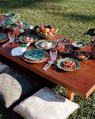 Fruit, charcuterie, salads and smoked salmon are served in green majolica plates and bowls at a picnic table on the lawn.