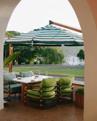 A cantilever parasol covers a table with four cushioned lounge chairs in blue and green on Y's garden- and falls-view terrace.