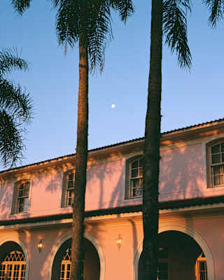 Tall palms spill shadows on the pink exterior of the hacienda-style Hotel Das Cataratas, glowing in rosy early evening light.