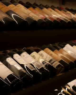 Close-up image of laid-down bottles of wine in long rows, labels facing upwards, seen in the wine cellar.