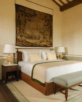 A vintage-look tapestry hangs above an immaculate bed with white linen and beige and green throw, with side tables and bench.