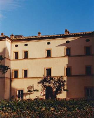 View over gardens of the exterior of Casello di Casole with three levels of doors and windows in warm honey-toned walls.