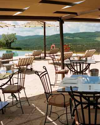 Castello Grill's terrace tables await lunch guests beneath a canopy shade in a view that captures the pool and rolling hills.