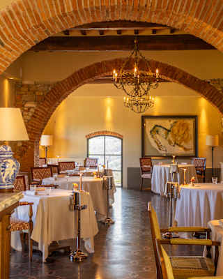 View past a marble bar to a warm-lit dining room with white-cloth tables, framed by two brick wall arches at Tosca restaurant.