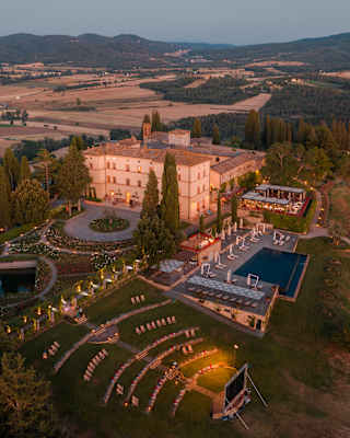 Magical aerial view of Castello di Casole at dusk, with the hotel, outdoor cinema and terrace illuminated with pretty lights.