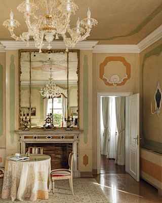 An enormous antique mirror reaches from the mantelpiece to the high ceiling, reflecting a painted ceiling rose and chandelier