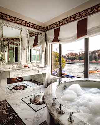 Soap bubbles fill the circular bath of a tub and russet marble bathroom. Outside large windows, the Hotel launch sets sail